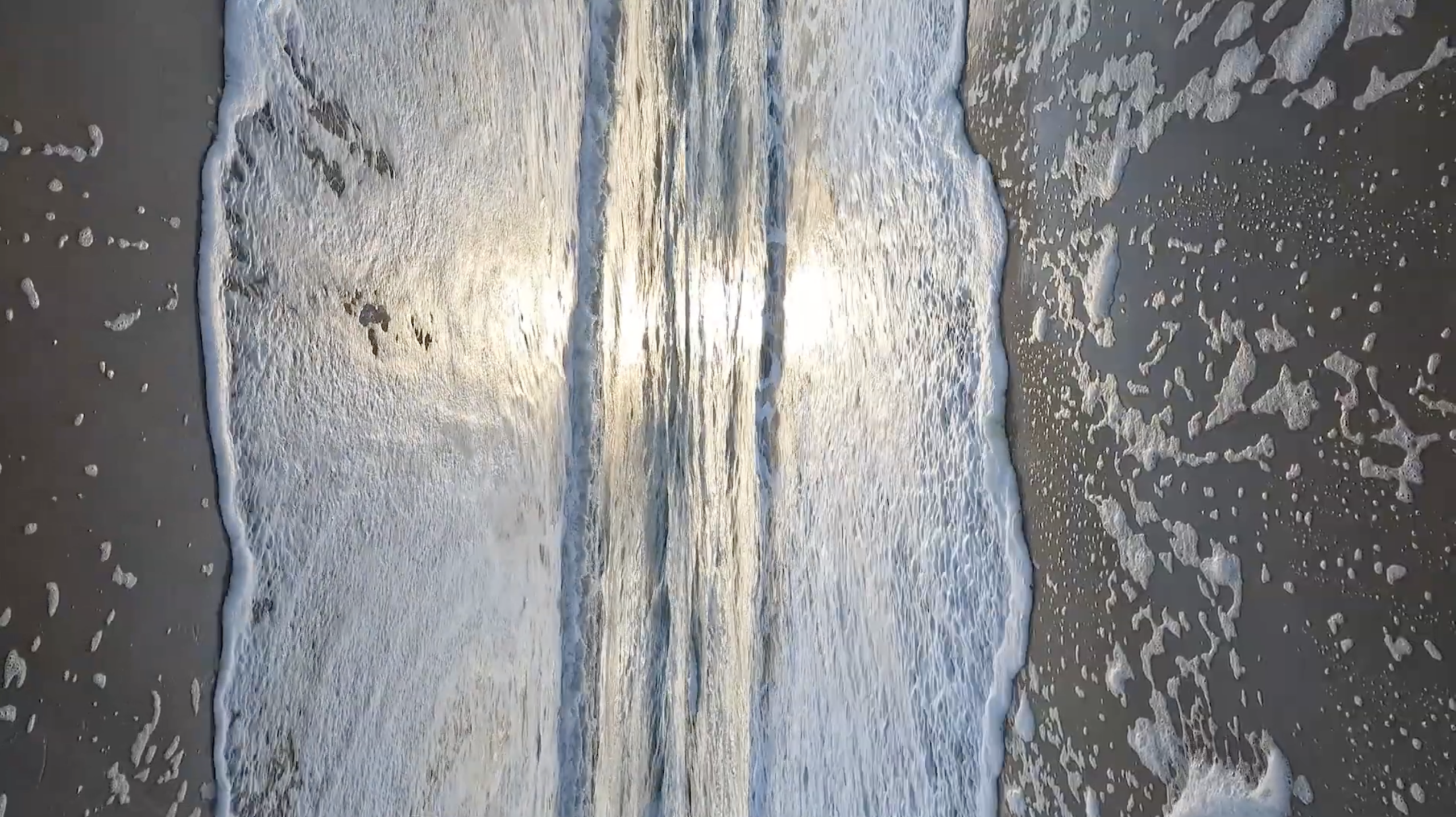 Golven die over zand spoelen, met witte schuimstrepen
