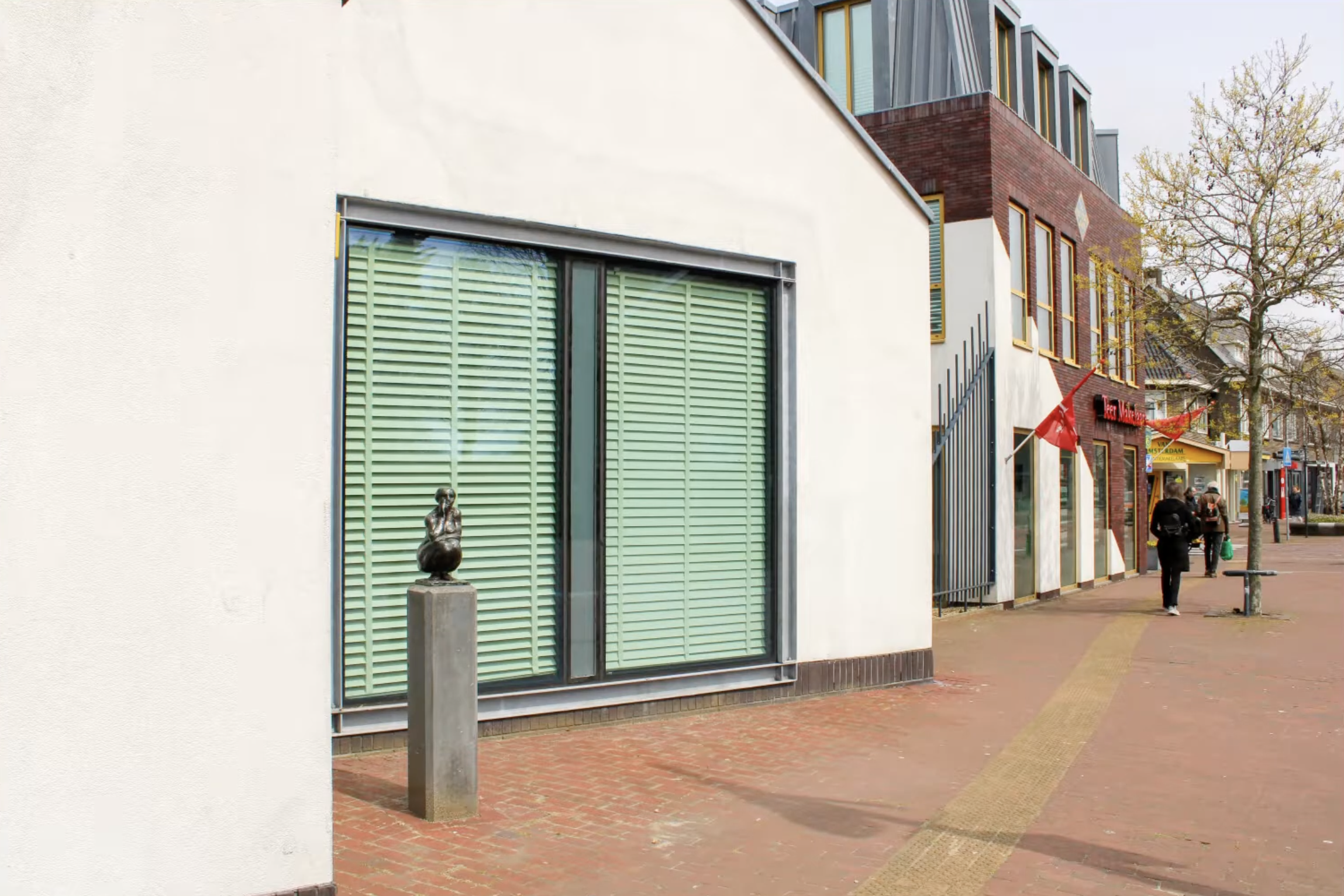 Bronzen vrouwenfiguur op stenen sokkel voor gebouw gevel