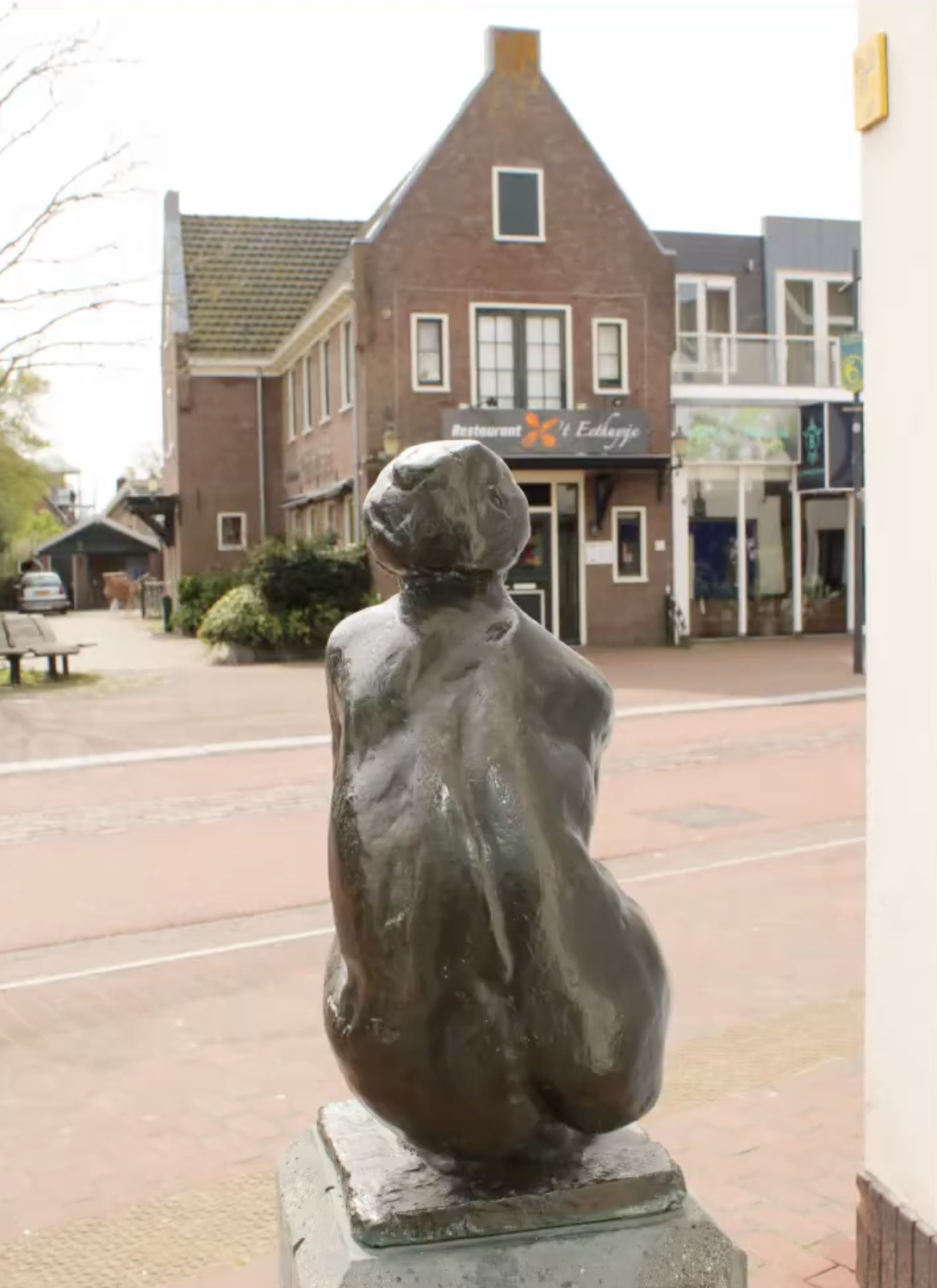 Bronzen vrouwenfiguur op stenen sokkel voor gebouw gevel