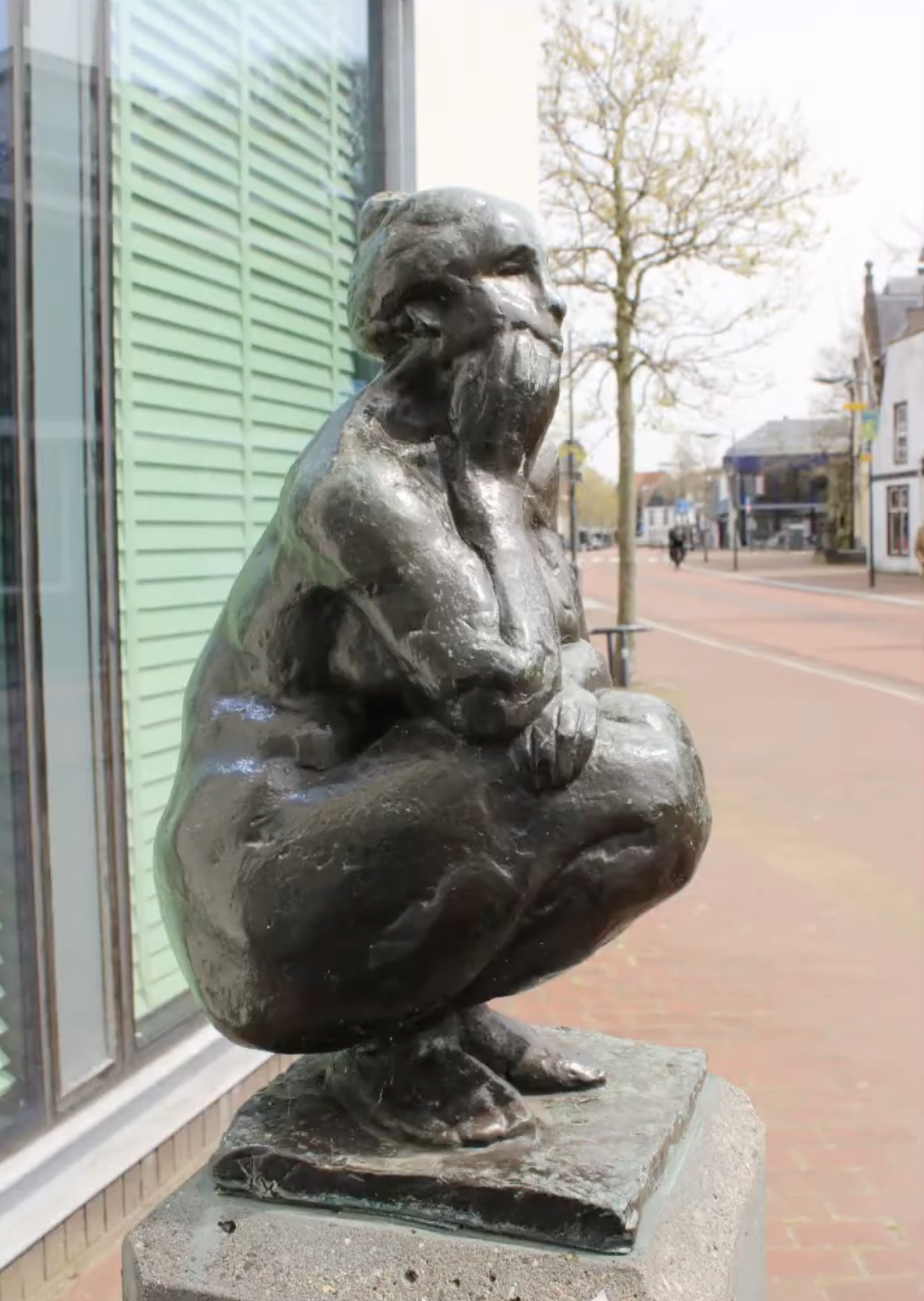 Bronzen vrouwenfiguur op stenen sokkel voor gebouw gevel