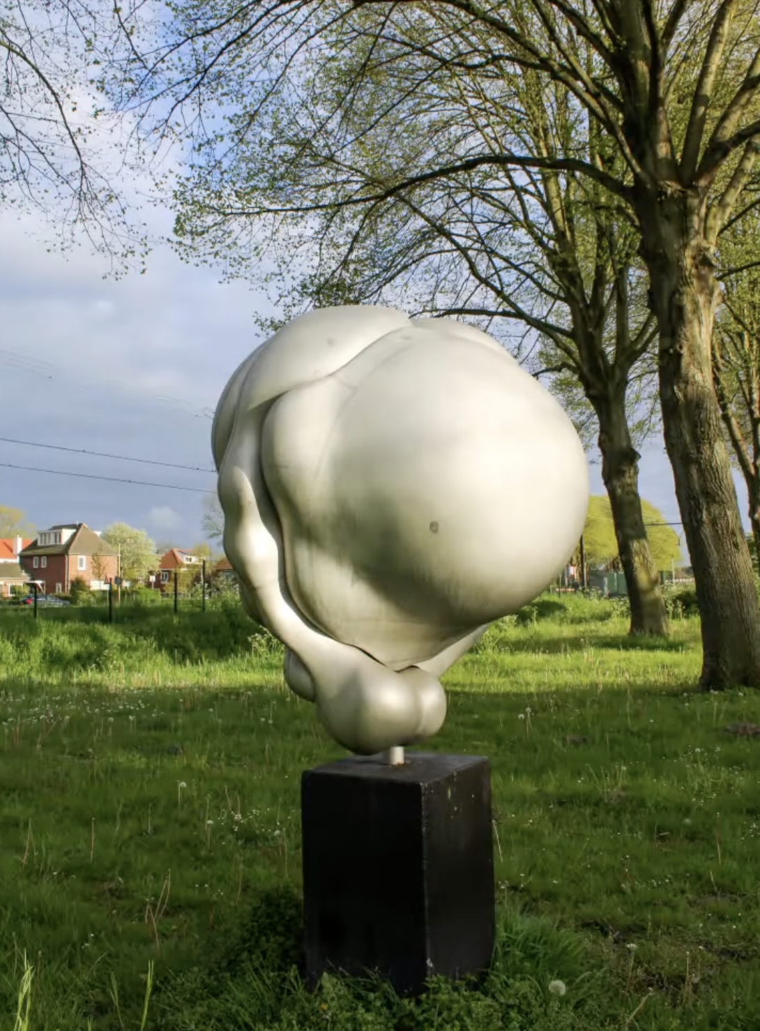 Een abstracte, witte sculptuur van organische, vloeiende vormen opgesteld in een groene buitenruimte met bomen op de achtergrond.