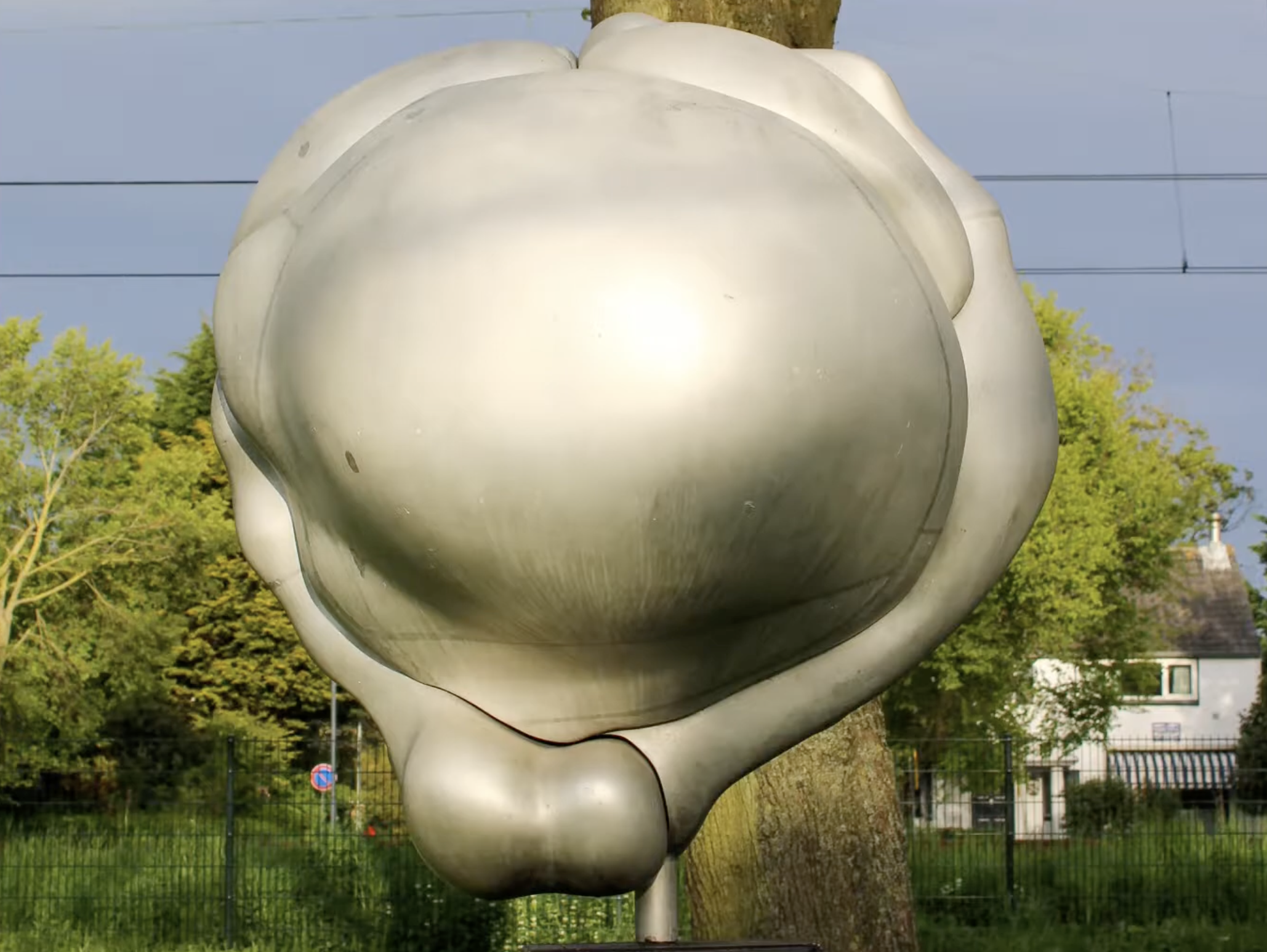 Een abstracte, witte sculptuur van organische, vloeiende vormen opgesteld in een groene buitenruimte met bomen op de achtergrond.