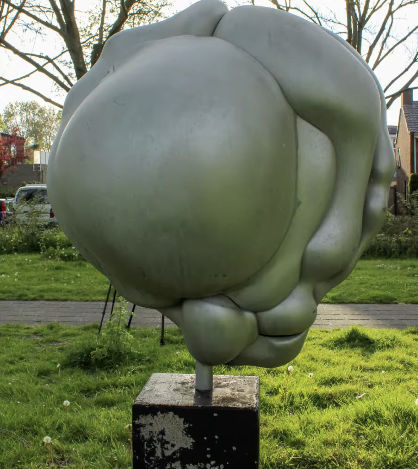 Een abstracte, witte sculptuur van organische, vloeiende vormen opgesteld in een groene buitenruimte met bomen op de achtergrond.