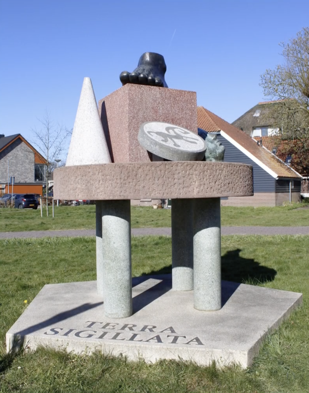 Abstracte sculptuur van terrazzo en brons op drie pijlers, met een voet, een kegel en een reliëfschijf, in een parkachtige omgeving.