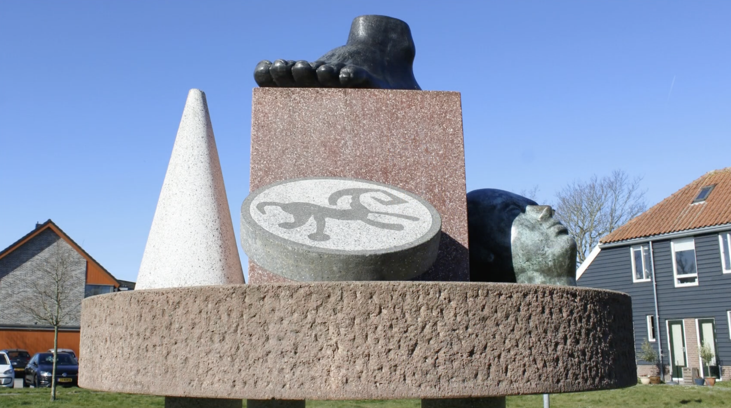 Abstracte sculptuur van terrazzo en brons op drie pijlers, met een voet, een kegel en een reliëfschijf, in een parkachtige omgeving.