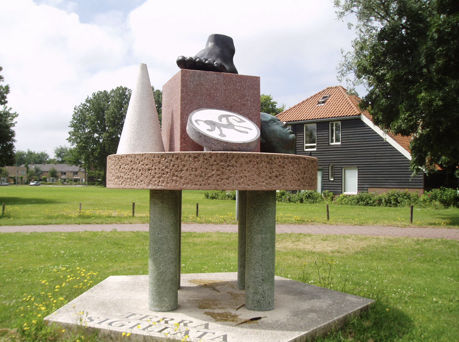 Abstracte sculptuur van terrazzo en brons op drie pijlers, met een voet, een kegel en een reliëfschijf, in een parkachtige omgeving.