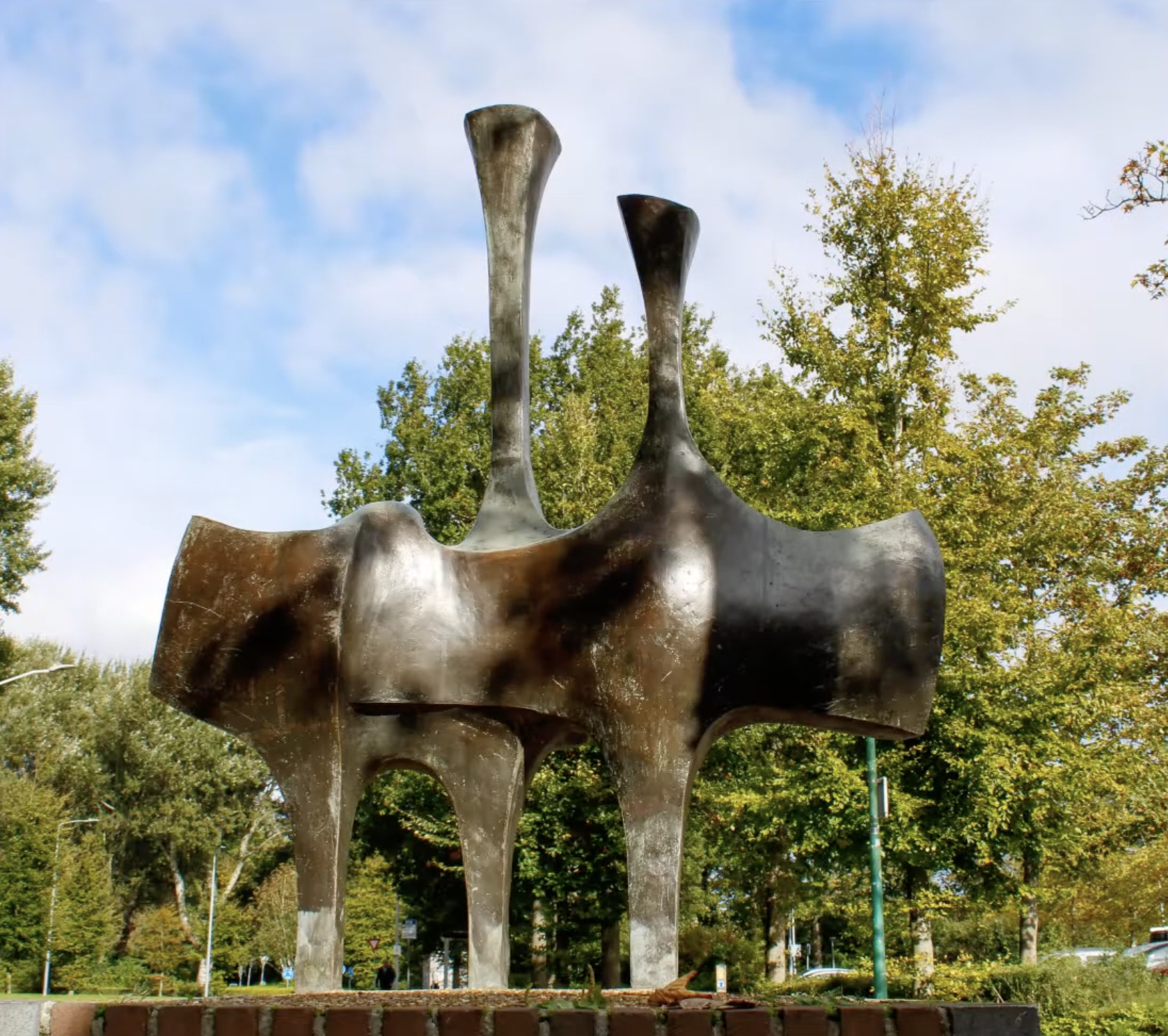 Abstracte bronzen sculptuur op een bakstenen sokkel bij een fietsenstalling in een Nederlandse stad.