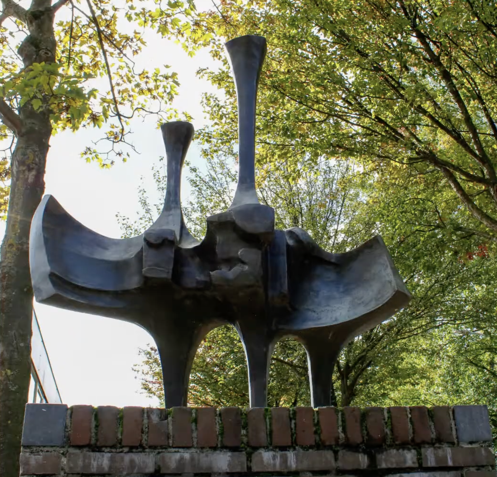 Abstracte bronzen sculptuur op een bakstenen sokkel bij een fietsenstalling in een Nederlandse stad.