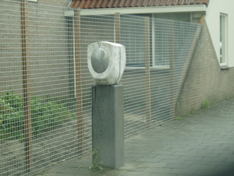 sculptuur van lichtgrijs/wit gevlekt marmer of natuursteen, bestaande uit een rond, schaalachtig vorm met een ovale verdieping in het midden, geplaatst op een rechthoekige grijze sokkel van beton of steen.
