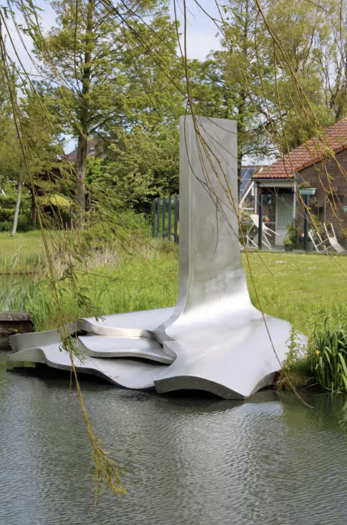 Een groot, glanzend roestvrijstalen kunstwerk in het water, met een golvend, organisch gevormd platform dat lijkt op een gestileerd blad of een gestold vel metaal, waaruit een hoog, gebogen verticaal element omhoog steekt.