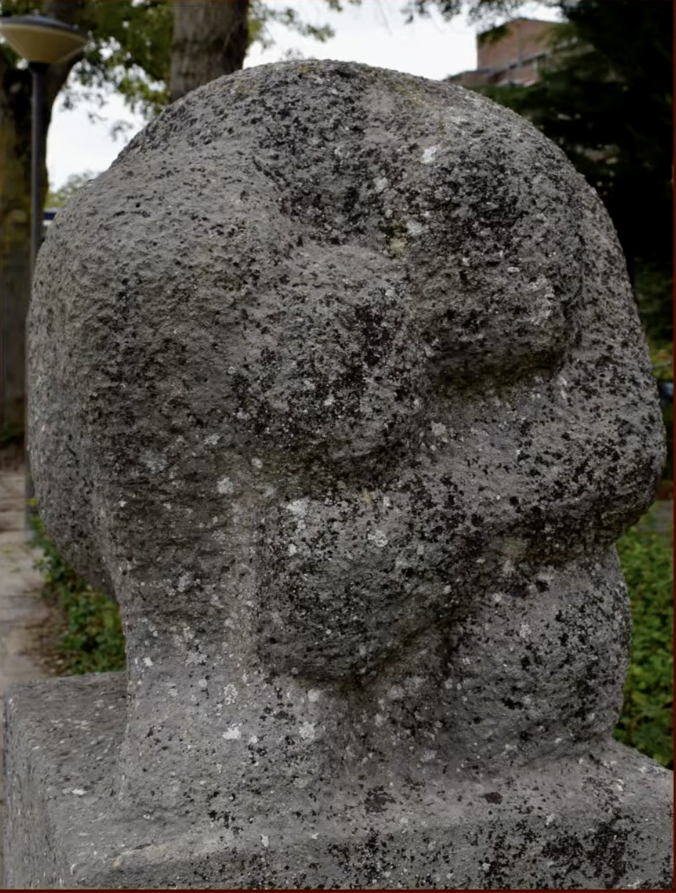 een stenen gedenkzuil met daarop een abstract gebeeldhouwd knoopvormig element van ruwe natuursteen.