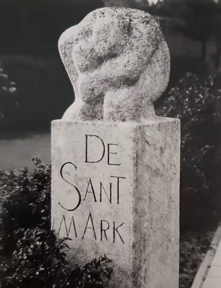 een stenen gedenkzuil met daarop een abstract gebeeldhouwd knoopvormig element van ruwe natuursteen.